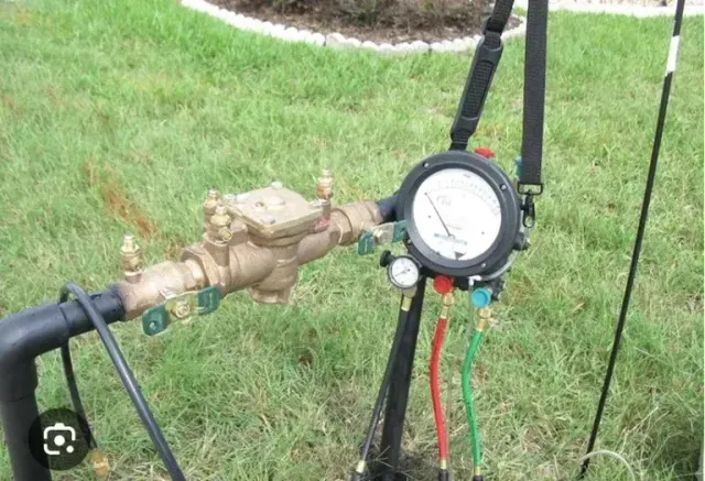 Water meter with gauges and connections on a grassy lawn.