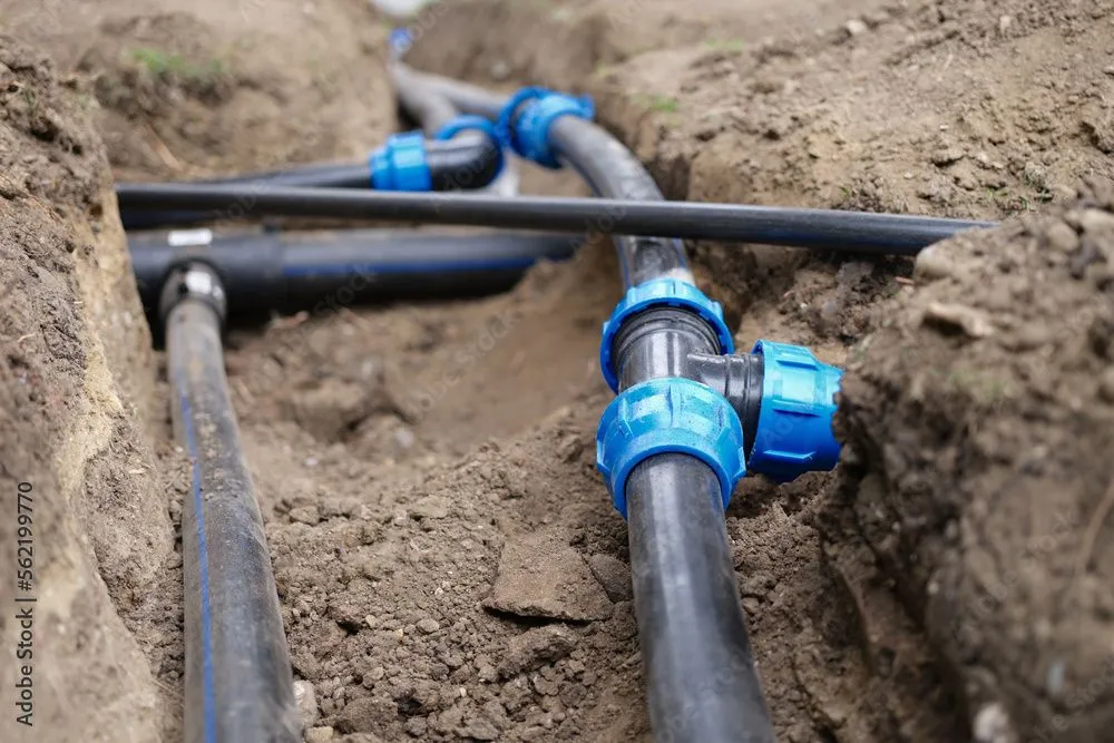 Black pipes with blue connectors installed in a trench, likely for a water system.